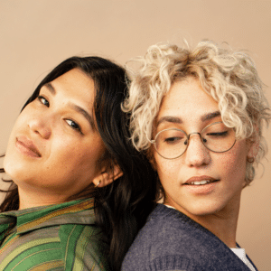 two people, one with long black hair and one with short curly blonde hair, standing together back to back