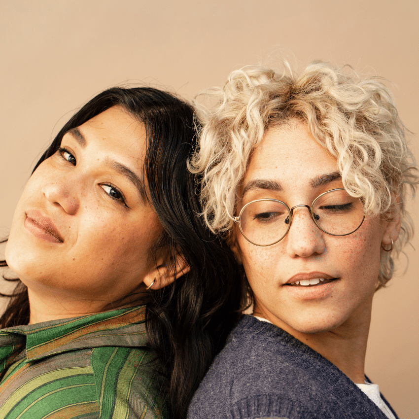 two people, one with long black hair and one with short curly blonde hair, standing together back to back