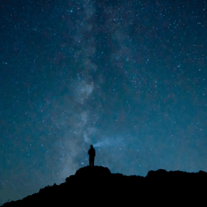 person standing on a large hill starring up at a blue starry sky