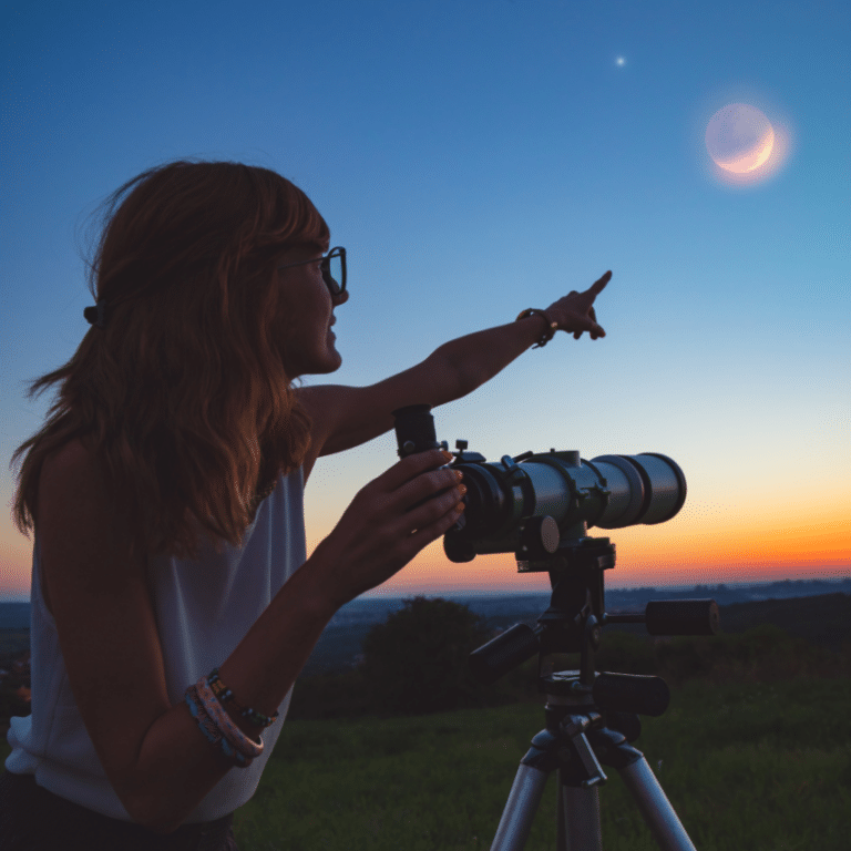 woman with glasses and a telescope pointing to a new moon in a blue and orange sky