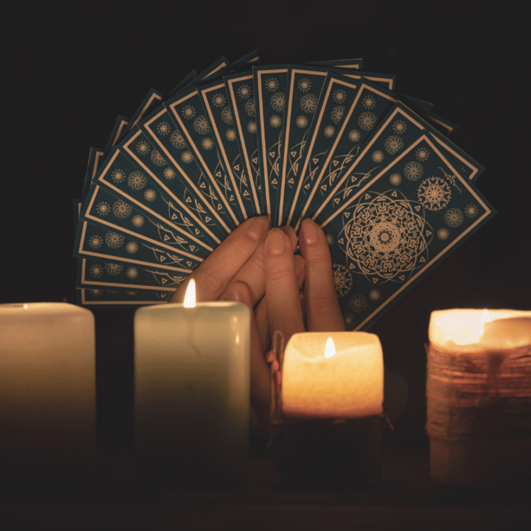 pair of hands holding up a spread of blue tarot cards behind a row of candles