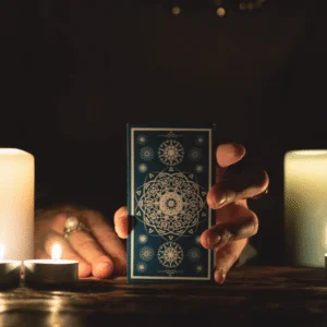 hand extended out holding a blue tarot card surrounded by white candles