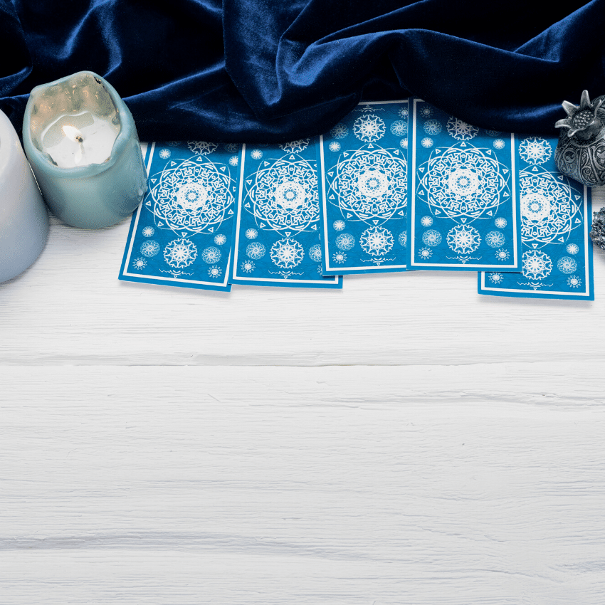 blue tarot cards spread across a white wooden table with candles and a blue velvet cloth