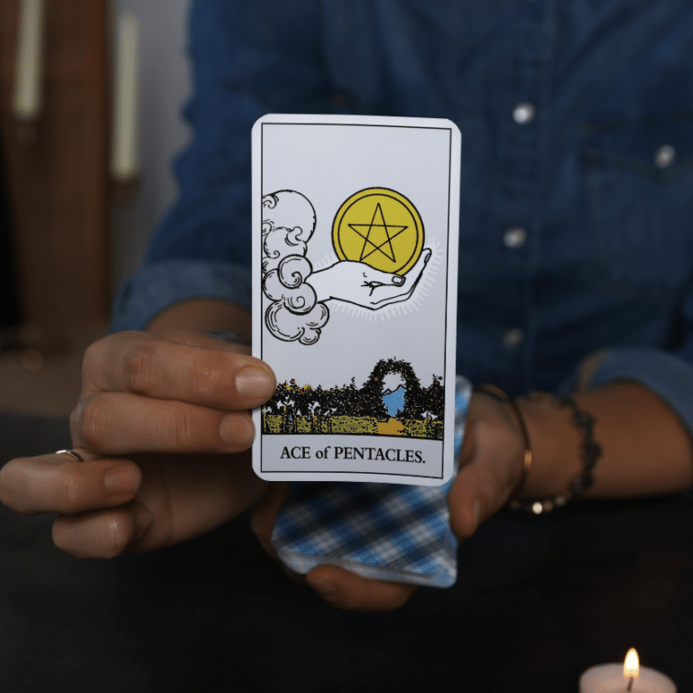 outstretched hand holding an ace of pentacles tarot card