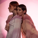 two eccentric woman with short hair dressed in light pink leaning against each other