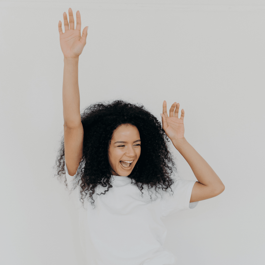 woman with black hair in white joyfully throwing her arms in the air