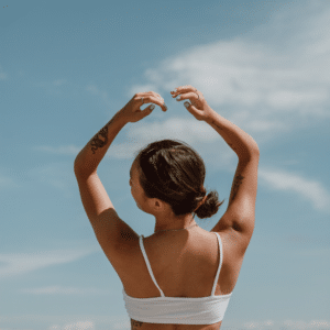 brunette woman in white sports bra with her arms outstretched to a blue sky