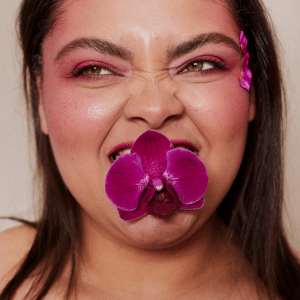 woman with pink eyeshadow holding a pink flower in her mouth