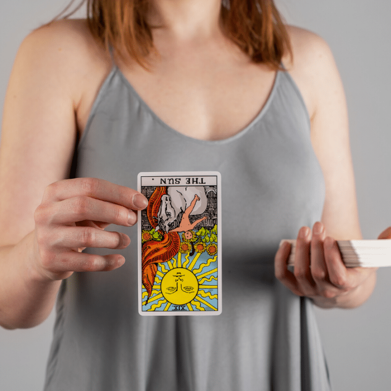 woman in a grey tank top holding out a reversed sun tarot card