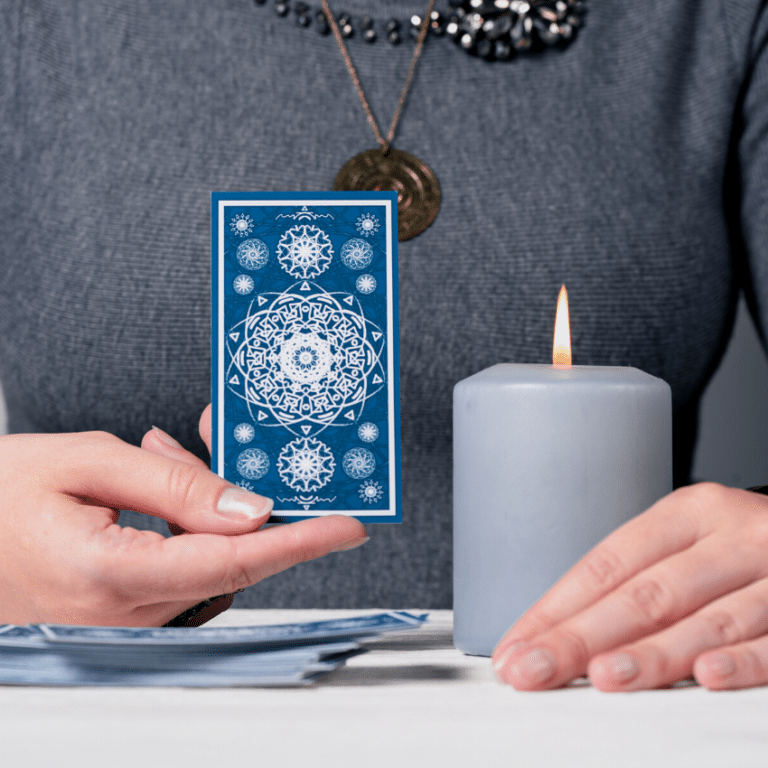 woman holding up a blue tarot card with a candle beside her