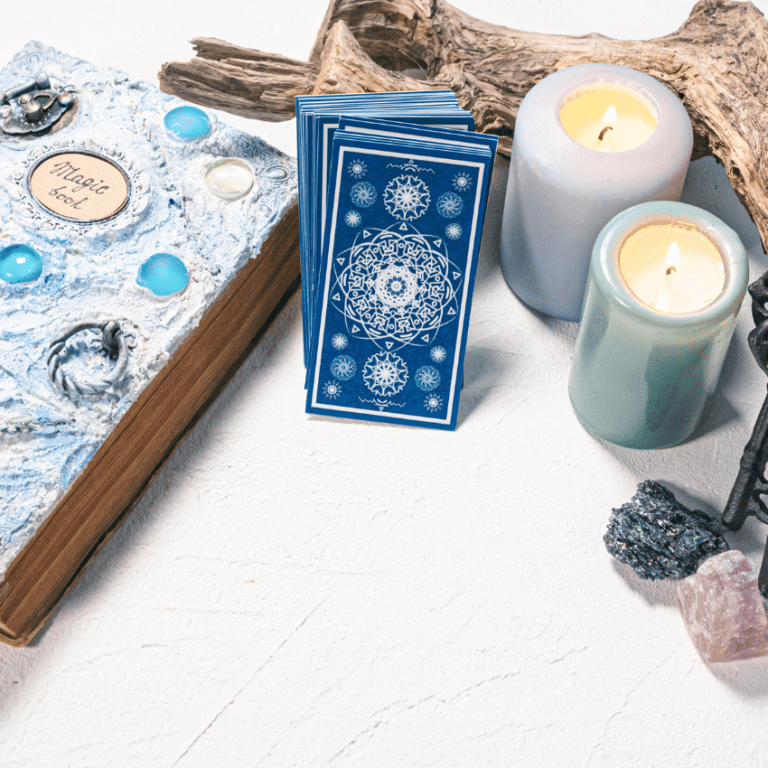 stack of blue tarot cards leaning against a blue book and candles on a white table