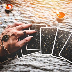 hand over top a spread of black tarot cards on a white cloth covered with red candles