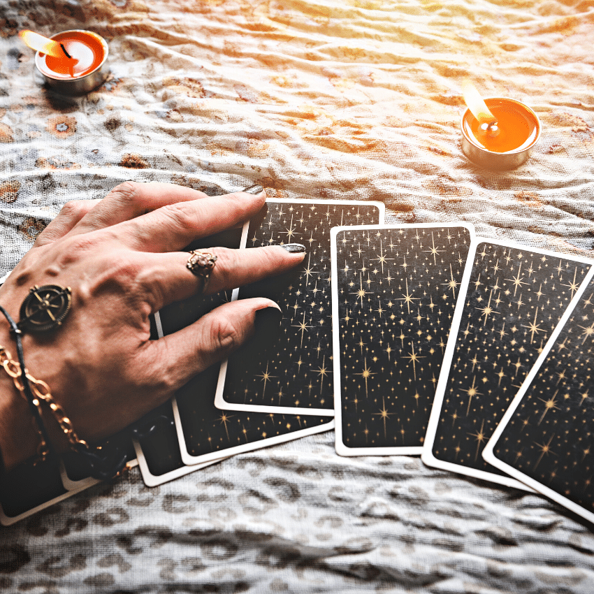 hand over top a spread of black tarot cards on a white cloth covered with red candles