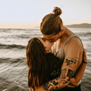 man and woman sharing a kiss in front of the ocean