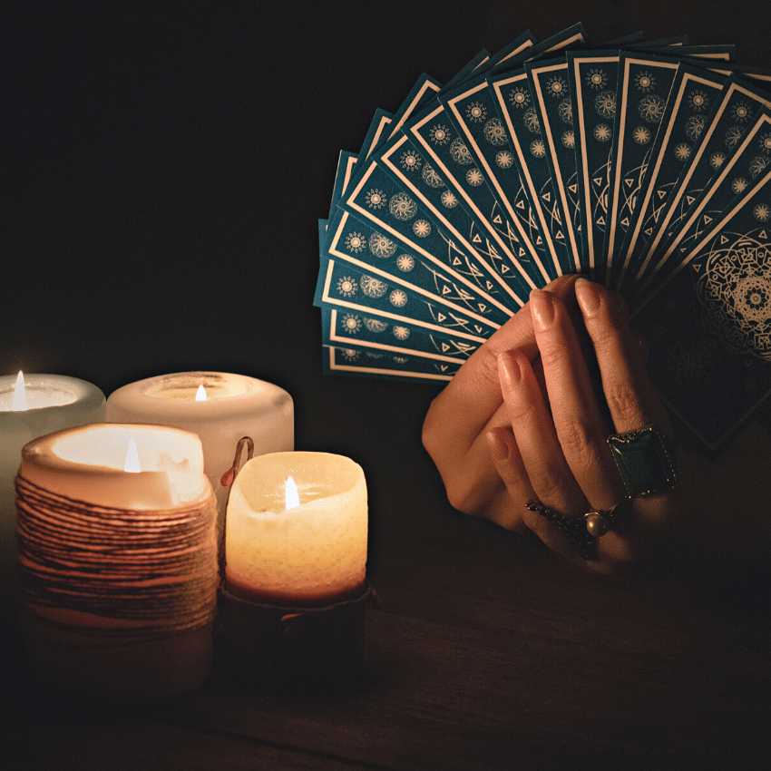 pair of hands holding up an array of blue tarot cards beside an assortment of candles