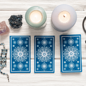 three blue tarot cards spread on a white table covered with candles and crystals