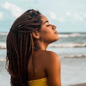 woman with dreadlocks on a beach with her eyes closed looking serene