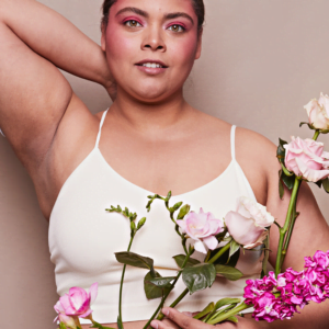 brunette woman in a white tank top and bold, pink eyeshadow holding an array of flowers