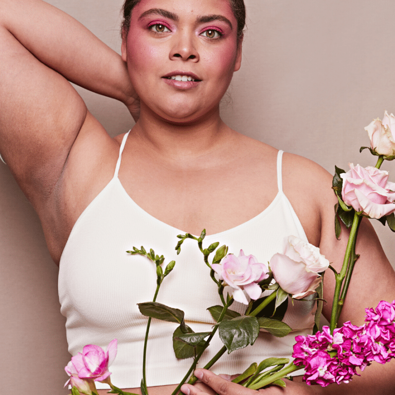 brunette woman in a white tank top and bold, pink eyeshadow holding an array of flowers