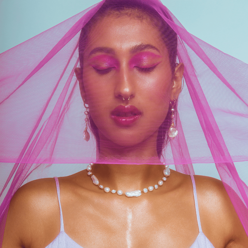 beautiful Indian woman adorned in jewellery and makeup with a pink cloth drapped over her head