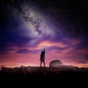 person standing on rocks with their arm outstretched toward a pink and purple starry sky