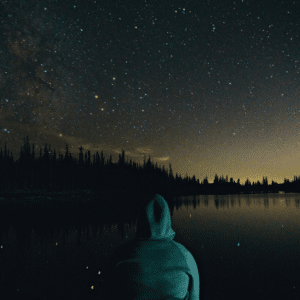 hooded figure staring ahead at a dark starry night