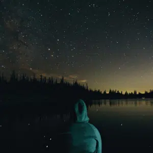 hooded figure staring ahead at a dark starry night