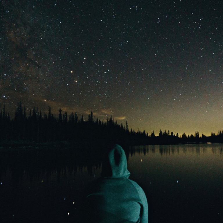 hooded figure staring ahead at a dark starry night