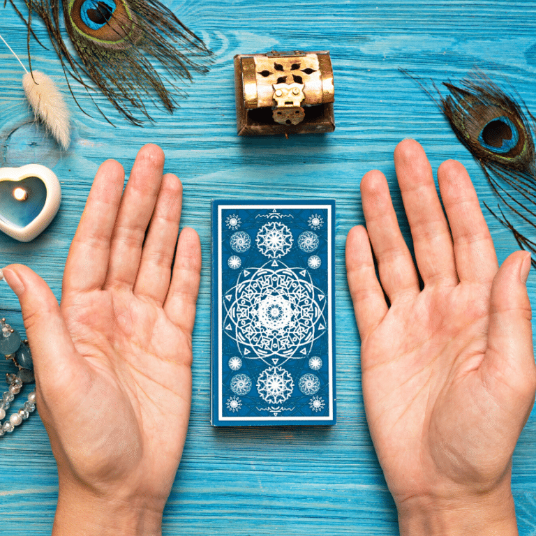 pair of hands outstretched beside a stack of blue tarot cards on a blue table