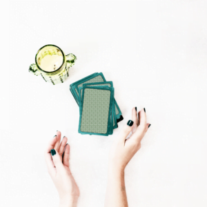 pair of hands outstretched on a white table toward a pile of green tarot cards