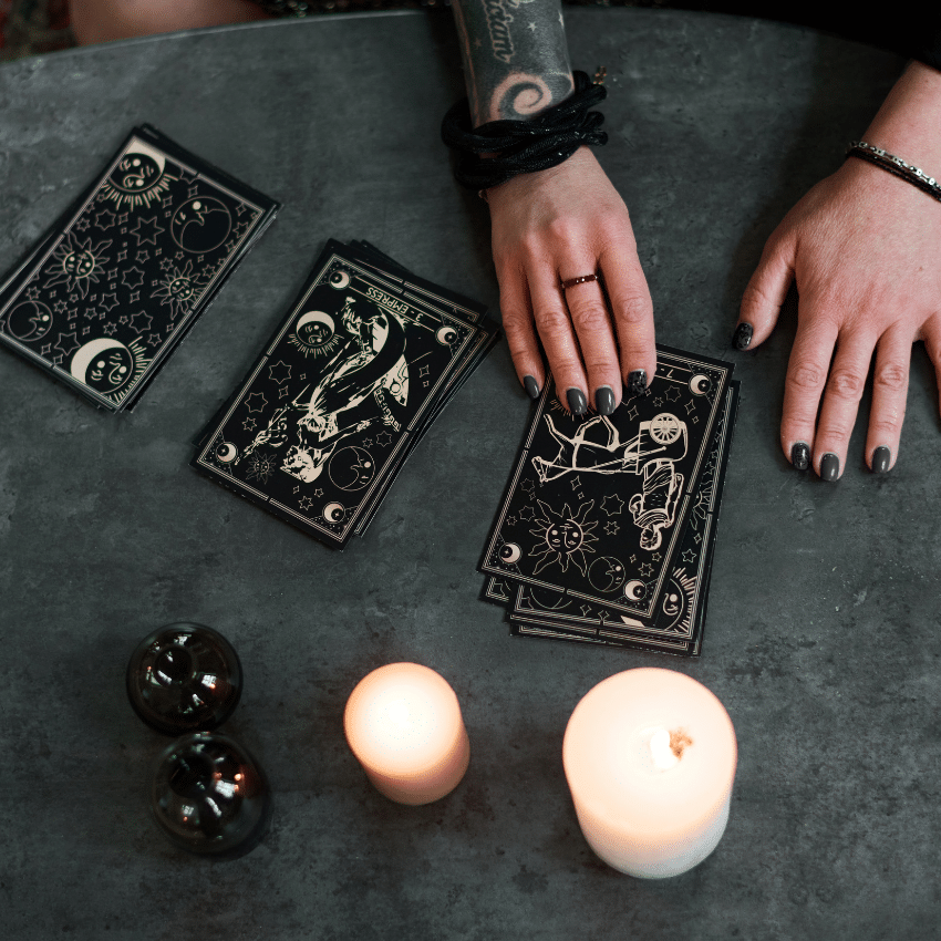 pair of hands dealing black tarot cards on a black table covered with white candles