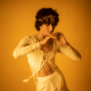 brunette person dancing in a gold outfit adorned with gold jewellery