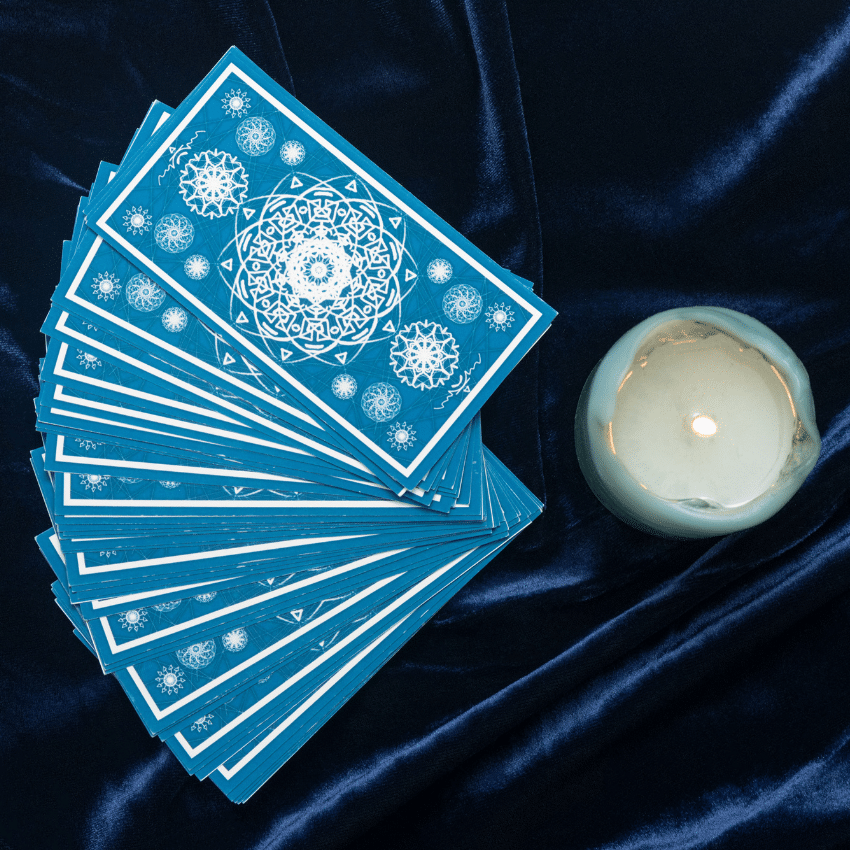 a deck of blue tarot cards spread out on a blue velvet cloth beside a candle