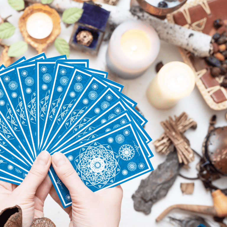 pair of hands holding out a spread of blue tarot cards over top a table covered with crystals and candles