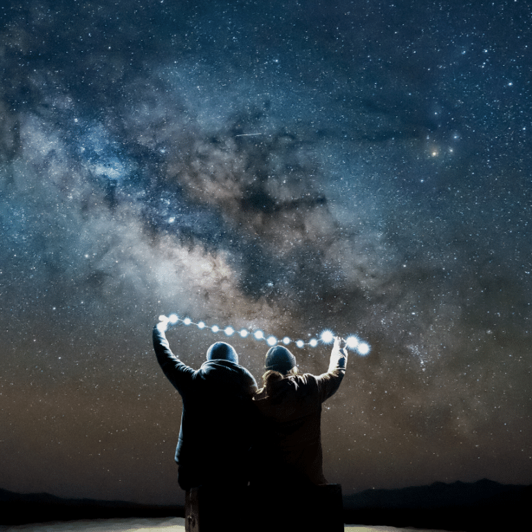 two people holding a string of lights against a backdrop of a blue and grey starry night