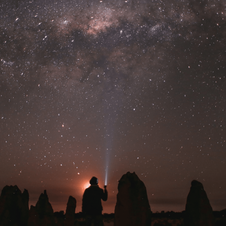 man shining a flashlight into a purple starry night