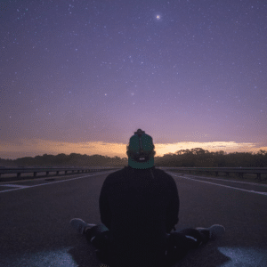 man sitting on the road gazing up at a purple starry night