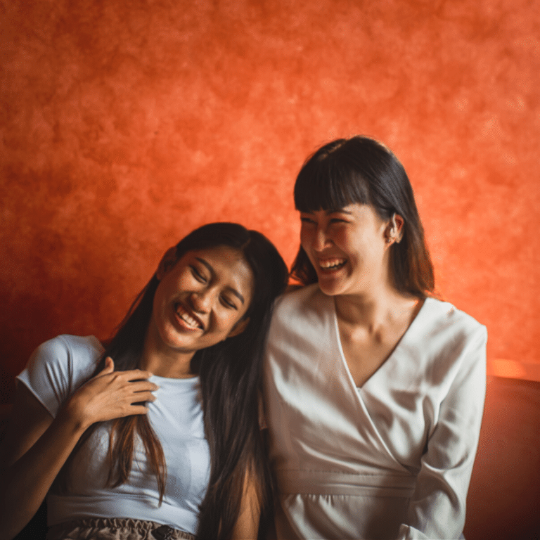 two friends laughing together against a burnt orange wall