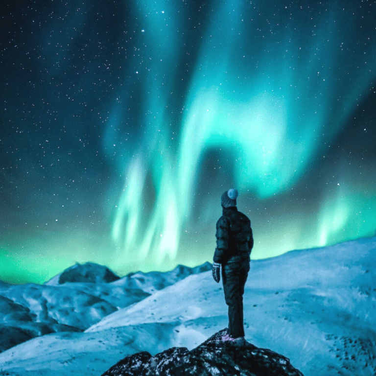person standing on a snowy hilltop gazing at the northern lights