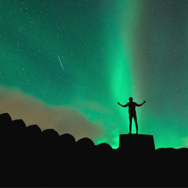 man standing on a staircase with his arms outstretched looking at a green starry sky