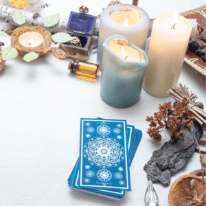 a stack of blue tarot cards on a white table beside candles and crystals