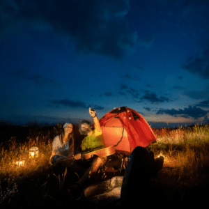 man and woman sitting outside of a tent gazing up at the stars