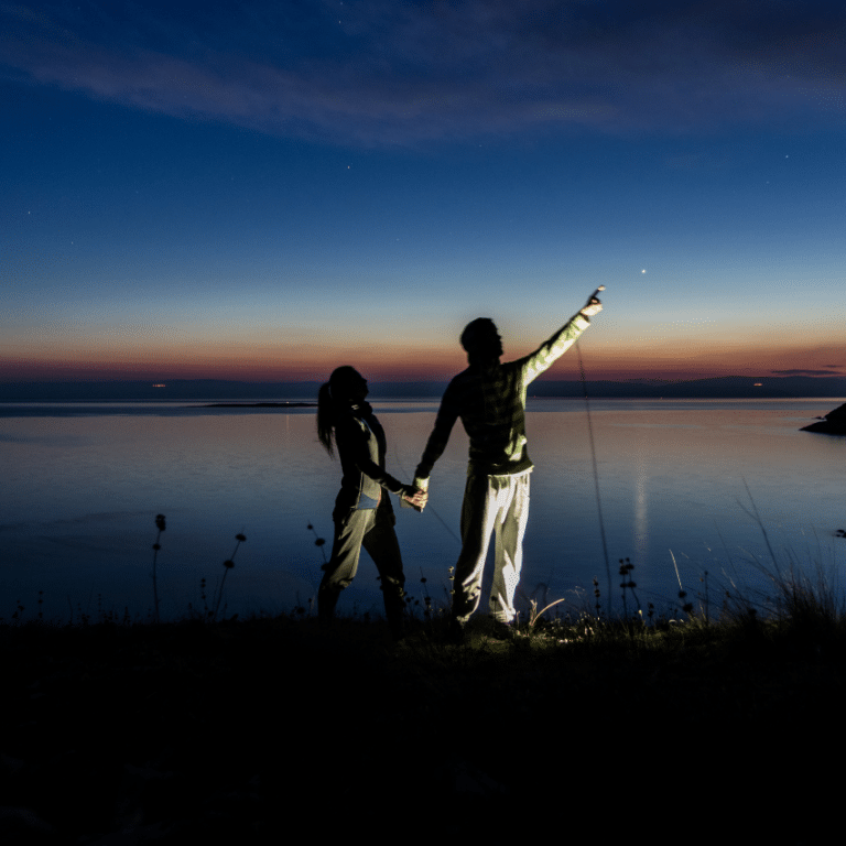 two people standing at the edge of a lake at night pointing up at the stars