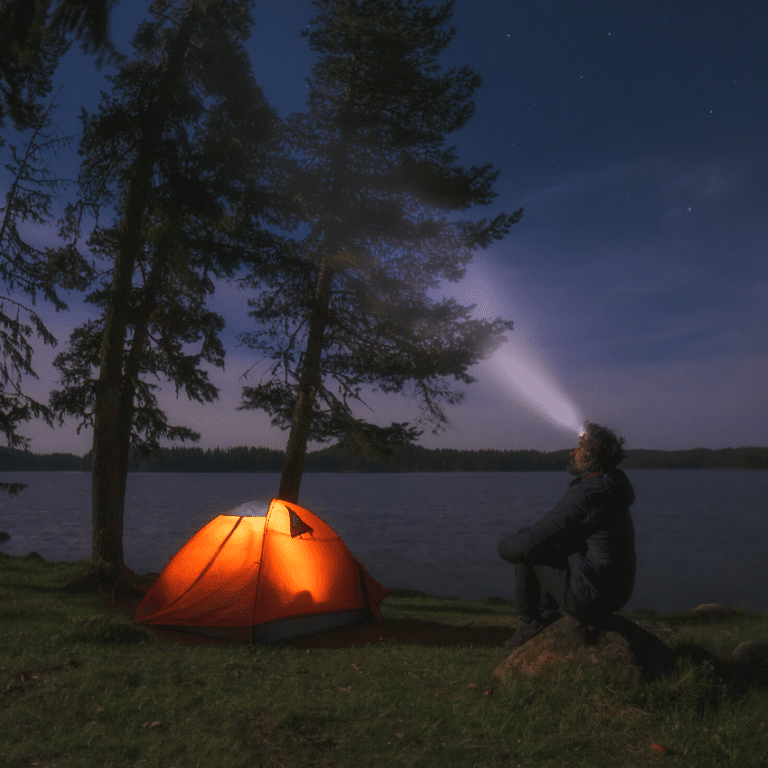 man sitting outside of his orange tent with a headlamp on gazing up at the sky