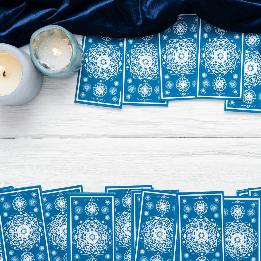 blue tarot cards spread out on a white wooden table with candles