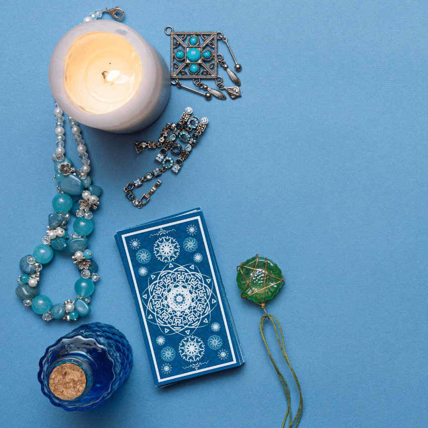 blue tarot card on a blue table surrounded by trinkets and candles