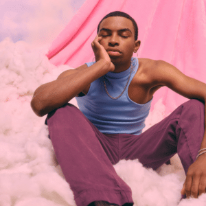 man sitting on a pink cloud in purple jeans and a blue tank top