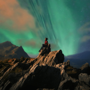 person sitting on a mountain top starring at the northern lights in the sky