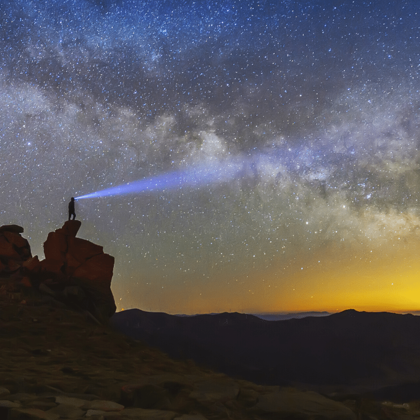 man standing on a cliffside with a headlamp gazing at the stars