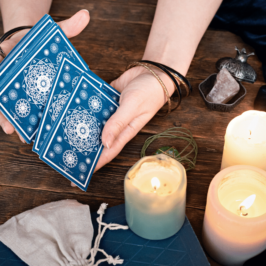 pair of hands shuffling blue tarot cards on a wooden table filled with candles and crystals